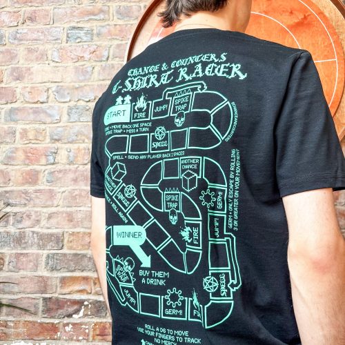Person wearing a black T-shirt with a large teal graphic on the back, standing against a brick wall.