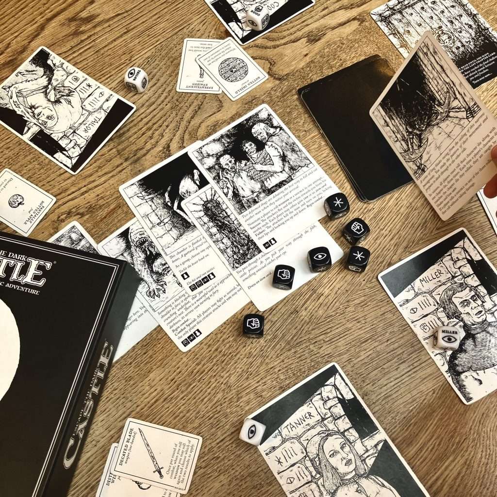 IMG_7056 - Chance & Counters Overhead view of a tabletop board game with illustrated black-and-white cards, dice, and a dark box on a wooden table