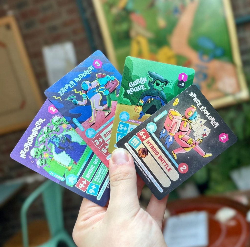 Hand holding five bright, illustrated game cards featuring space/fantasy characters and labels like 'Zapper Buddies', 'Goblin Rogue', and 'Space Explorer'