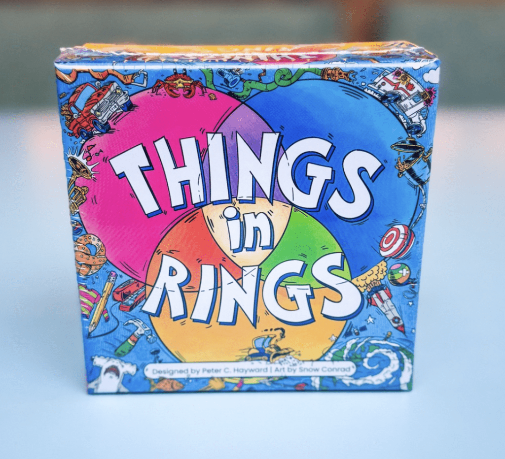 Box of the game 'Things in Rings' with a bright multicolored circular design and cartoon edges around it.