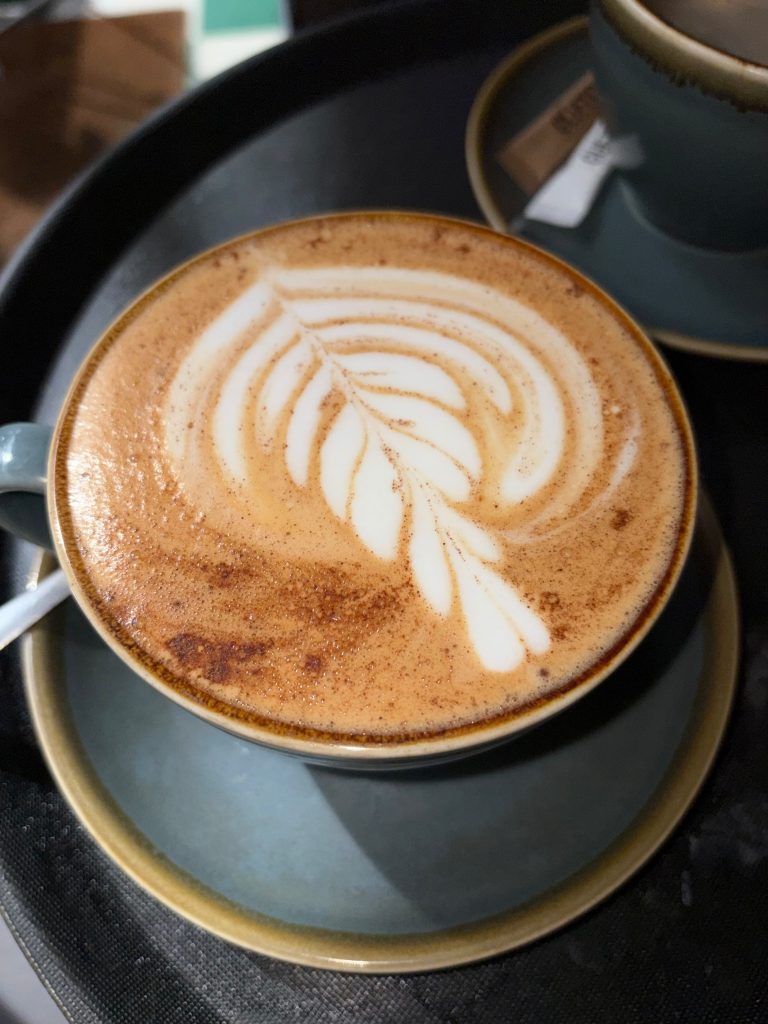 Latte with leaf-shaped latte art in a ceramic cup on a saucer.
