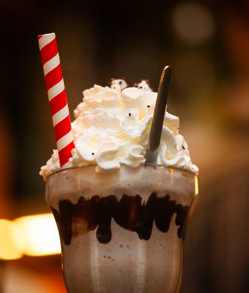Milkshake topped with whipped cream and a red-and-white striped straw in a glass.